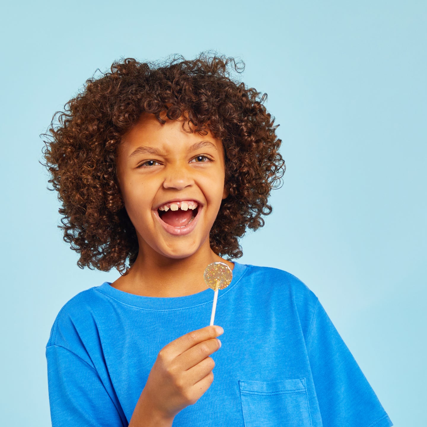 Kid smiling holding a Lolleez pop on a light blue background